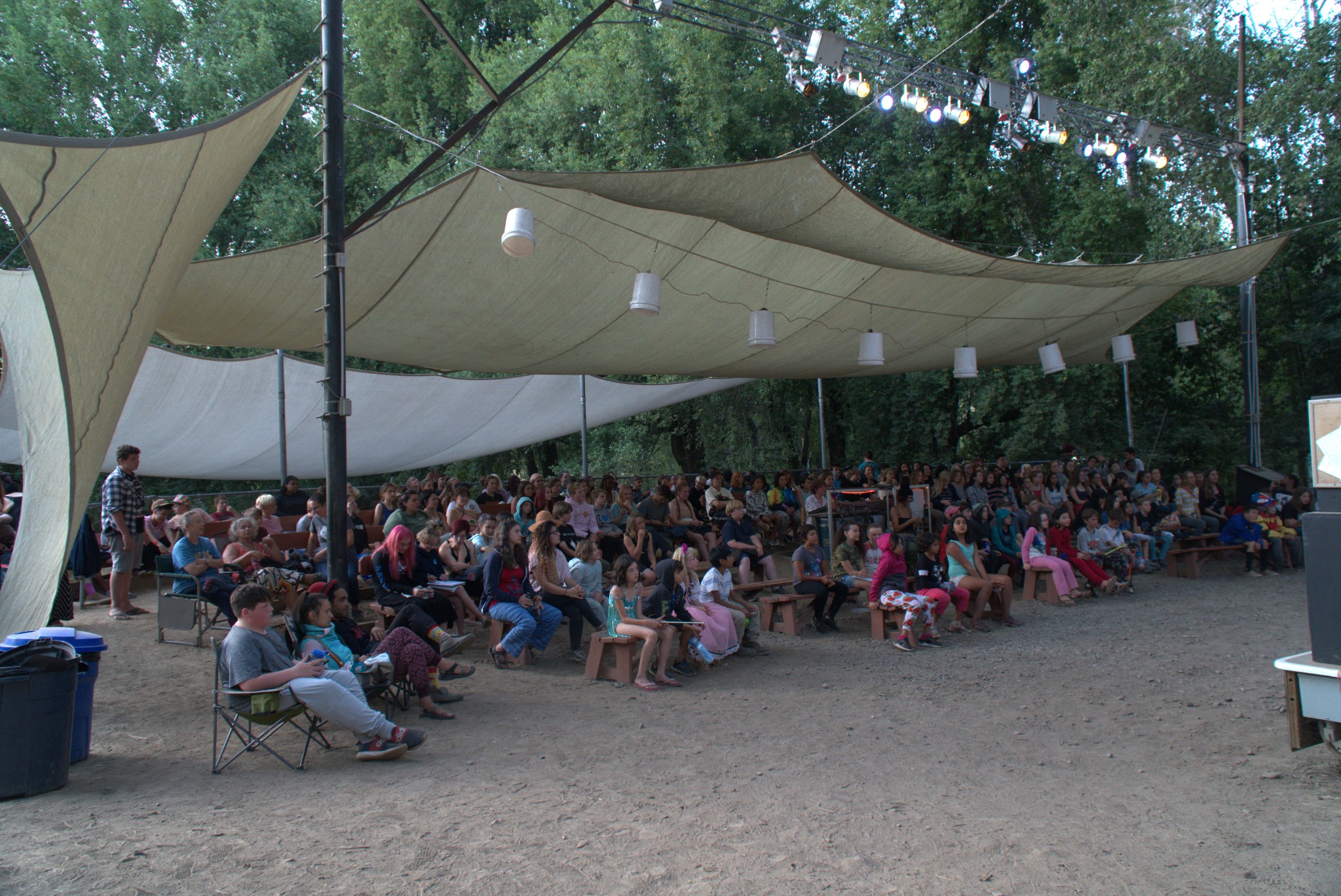 Audience gathered under shade structures at Camp Winnarainbow