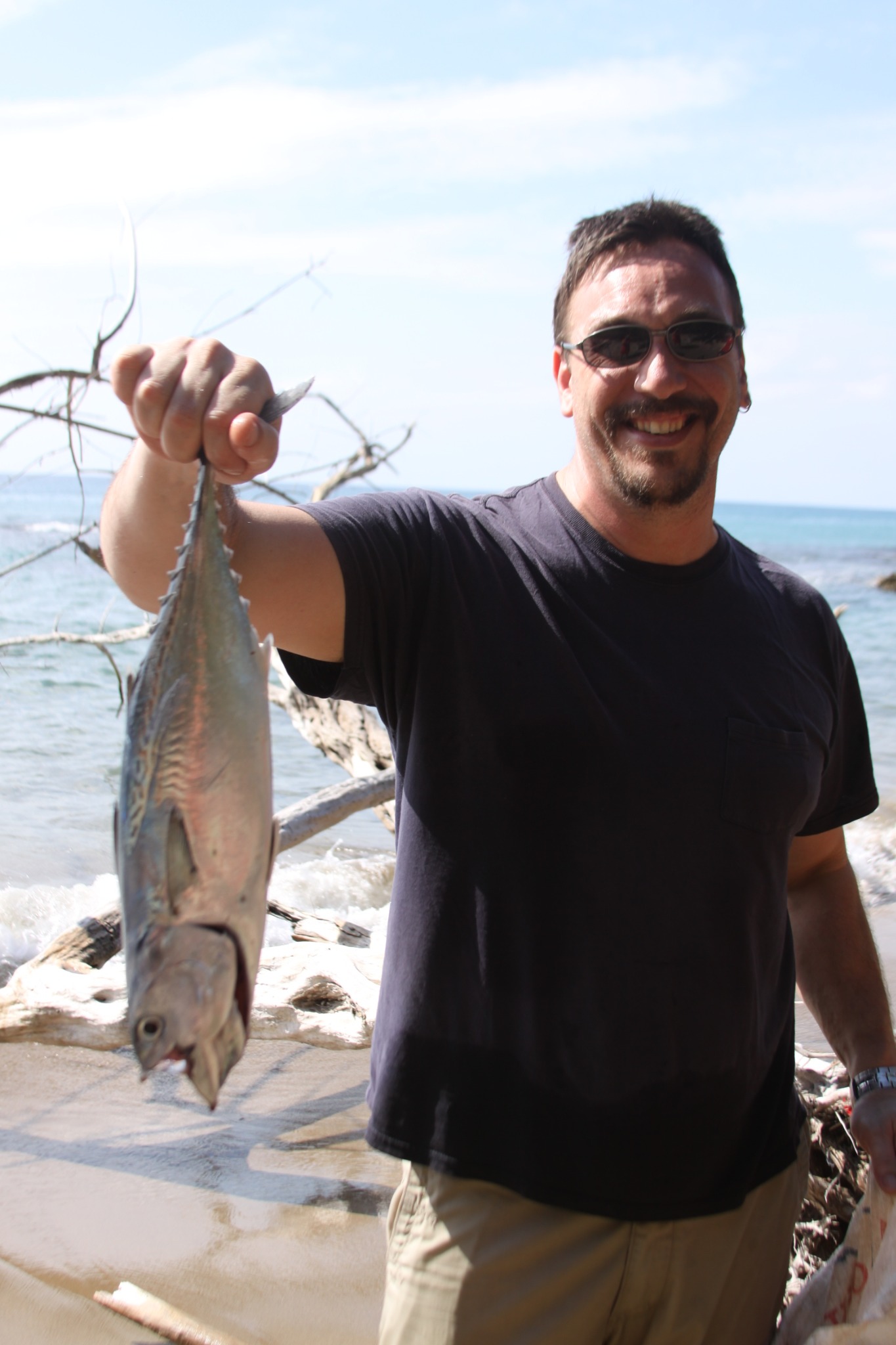 Micah Owens smiling and holding a fish on a beach